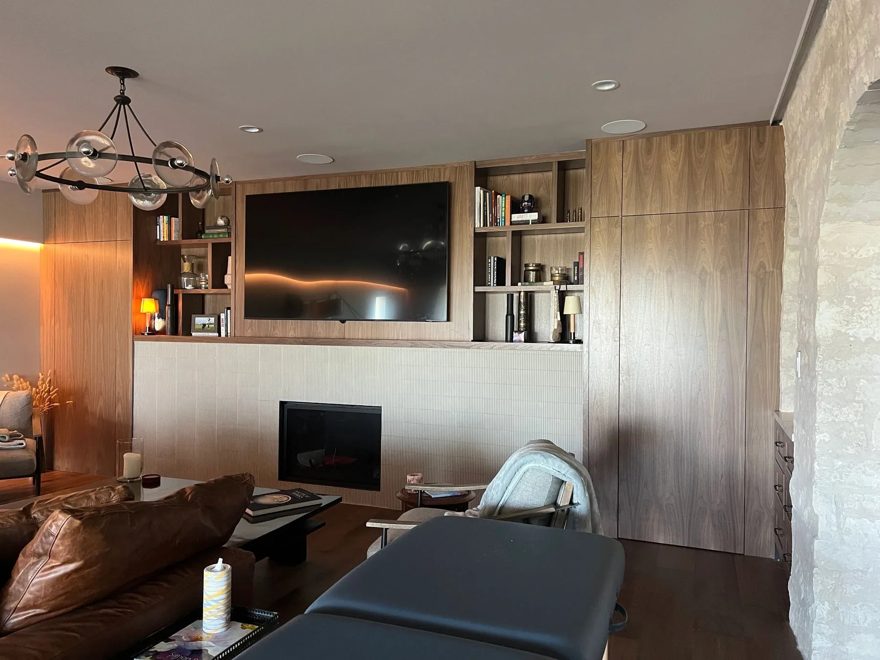 Walnut media wall with built-in TV, floating shelves, and tiled fireplace surround by Westcreek