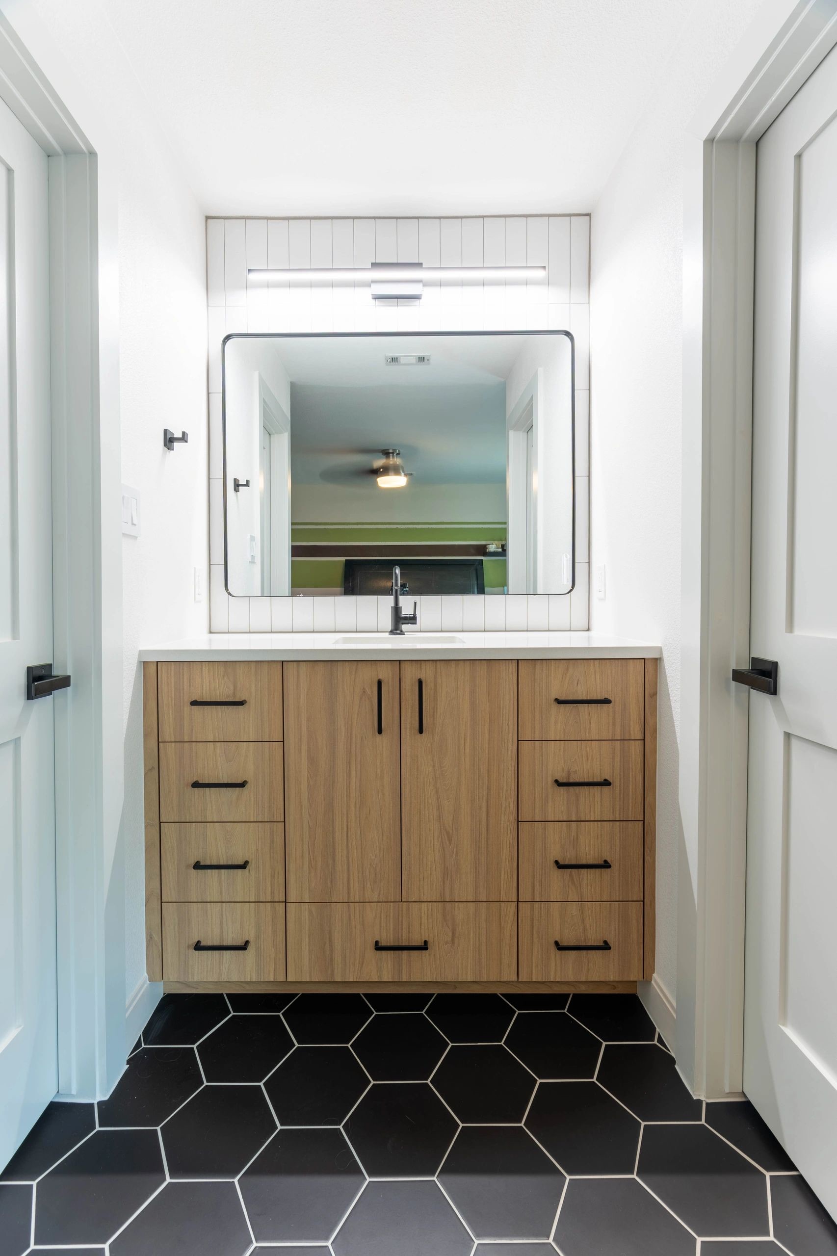 Wood vanity with black hexagon tile floor and black framed mirror by Westcreek