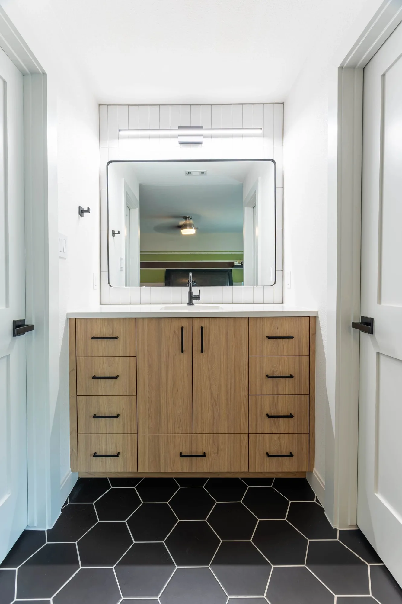 Wood vanity with black hexagon tile floor and black framed mirror by Westcreek